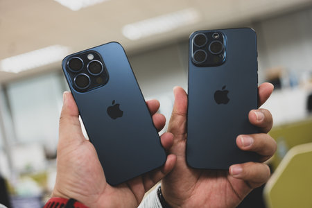 Bangkok, Thailand - December 12, 2023 : Two men holding iPhone 15 Pro Max is blue Titanium and iPhone 15 Pro is blue Titanium to compare. A tech smartphone modern design and the latest iPhone.のeditorial素材