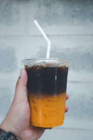A glass of coffee mix orange juice with ice in young hand on a cement background.の写真素材