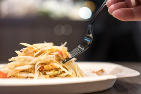 Spicy green papaya salad or Somtum, eating with black fork.の写真素材