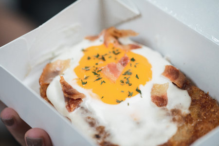 Hash brown topping with egg and bacon in paper box. Close upの写真素材