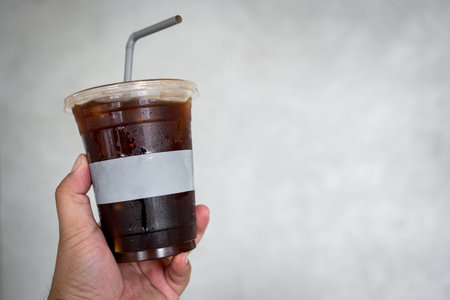 Iced black coffee, Closeup shot of man holding a plastic glass of coffeeの写真素材