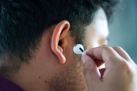 Bangkok, Thailand - December 24, 2023 : Busnessman holding AirPods 3 wireless Bluetooth in-ear headphone designed by Apple Computers inserting his earのeditorial素材