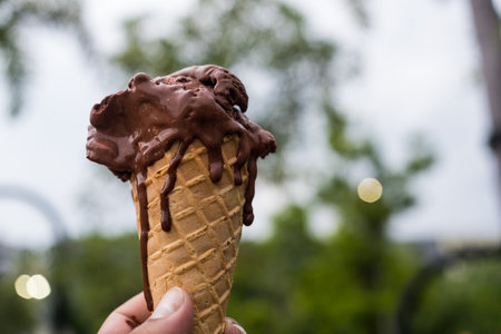 Melting chocolate waffle cone ice cream in a hand against nature backgroundの写真素材
