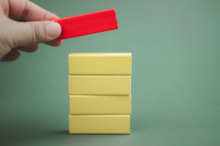 Hand putting red wooden block on top of other yellow wooden blocks. Customizable space for text. Copy space.の写真素材