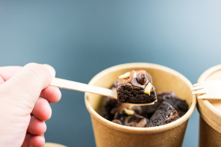Hand scoop by wood spoon a piece of delicious chocolate brownie topping with almond and chocolate chip from a bowl paper brownの写真素材