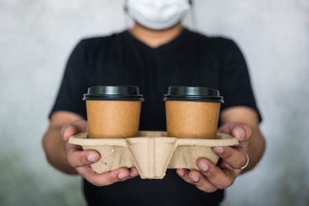 A waitress wearing a face mask handling two hot coffee cup to a customer in cafeの写真素材