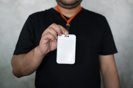 Male hand showing blank white badge on grey background, a blank security identity name card or tagの写真素材