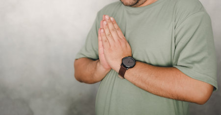 Close up of young man in green t-shirt greeting by doing namaste with folded hands in greeting pose. Hand symbol means to pay respect and greeting others.の写真素材