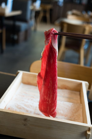 Hand picks a premium rare slices of beef with marbled texture with chopsticks from a wood tray. Served for Yakiniku and Shabu.の写真素材