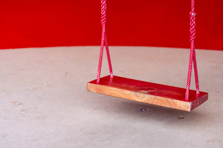 Wooden red swing for entertaining the smallest boys and girls. The empty red swingの写真素材