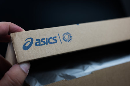 Bangkok, Thailand - January 19, 2024 : Hand open box with logo of ASICS in brown box. apanese multinational corporation athletic equipment company which produces footwear and sports equipmentのeditorial素材