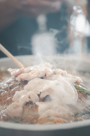 Hand with chopstick cooking Thai bbq pork at family dinner.