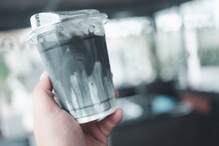 A man hand holding plastic cup of charcoal latte teaの写真素材