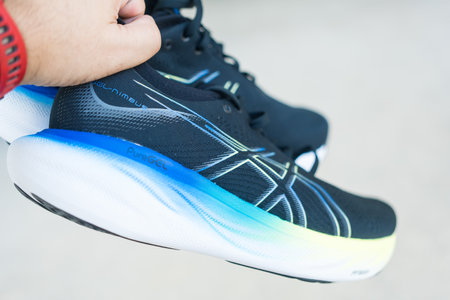 Samut Prakan, Thailand - February 8, 2024 : Man hand holding a shoe of ASICS Running Shoes Gel Nimbus 25 WIDE. Shoe sport sneakers for joggingのeditorial素材