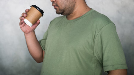 Green T-shirt men drink paper cup hot. Handsome man with cup of coffee in handsの写真素材