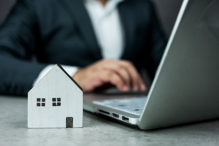 Businessman working on a computer with a white wooden house model in front of them. Smart home technology concept. Concept of rent, search and purchase real estate.の写真素材