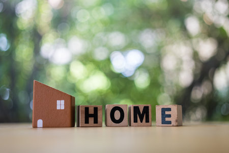 A brown model of a house and text HOME in wood block against nature background with copy space for your text.の写真素材
