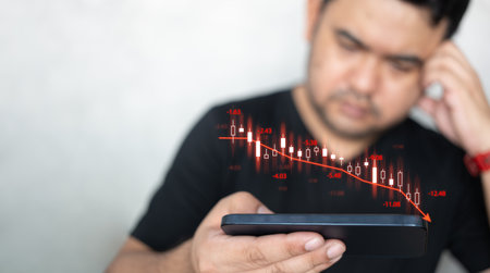 Man using mobile phone checking stock market graph report via mobile apps trading decreasing chart data fall down. Upset by fall in value shares. Decline in share price. Losing money on stock exchangeの写真素材