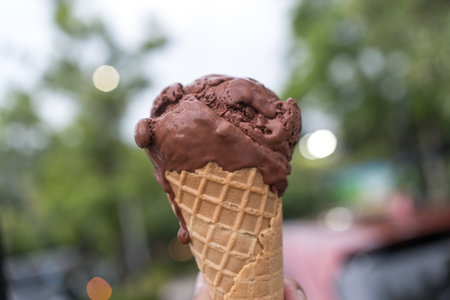 Chocolate ice cream cone on hand against nature background