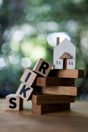 Wood house on wood tower with text of RISK fall over, money risk management in financial, foreclosure and bankruptcy concept.の写真素材
