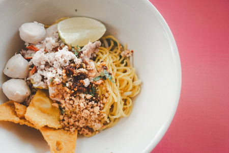 Egg noodles dried egg noodles with lime, minced pork, meatballs, and fried dumplings in white bowl. Asian food styleの写真素材