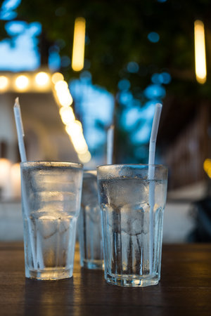 Very cold mineral water with ice and white straw on the wood table at restaurantの写真素材
