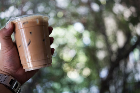 Iced coffee disposable plastic cup in hand against nature backgroundの写真素材