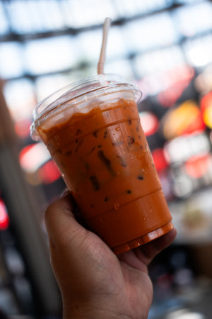 A cup of the ice thai milk tea with a plastic tube in hand. Iced fresh Thai milk tea made from real tea leaves, popular menuの写真素材