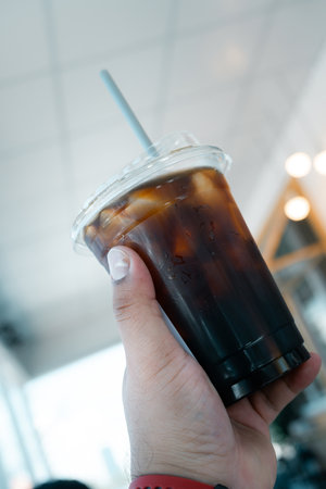 Man holding a plastic iced black coffee in the coffee shopの写真素材