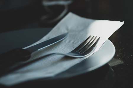 Metal knife and fork on a tissue paper and dish on a wooden table. Near white dishes. The concept of foodの写真素材