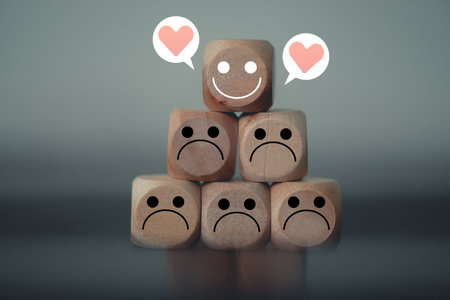 Happy face with heart icons among many sad emotions on wooden blocks. Happy leader among negative team. Individuality. World mental health day. Human development, psychology personality concept.の写真素材