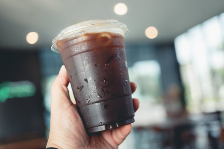 Someone hand holding a plastic cup of iced Americano at the cafe