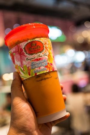 Samut Prakan, Thailand - May 29, 2024 : Hand holding a glass of iced Thai milk tea from the famous of Thai tea branding Cha Tra Mueのeditorial素材