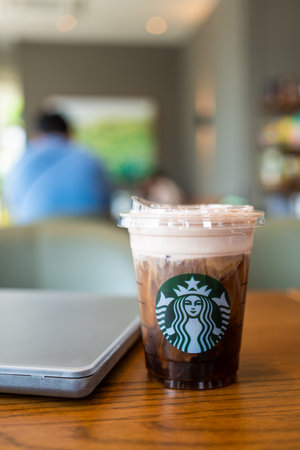 Samut Prakan, Thailand - May 21, 2024 : Starbucks cold brew beverage cup on wood table with computer notebook. Starbucks is the world's largest coffee house with over 20,000 stores in 61 countries.のeditorial素材