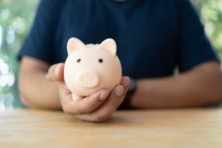 Man is holding pink piggy bank on wood table, saving money wealth, financial, business, finance, investment and financial planning. Symbolizing commitment to saving for futureの写真素材
