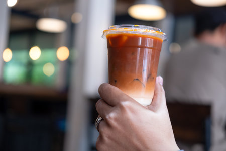 Hand holding glass of iced Thai milk tea. Thai milk tea is a traditional Thai drink that has long been popular.の写真素材