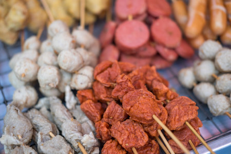 Various fried skewers meatballs and sausage. Selection of inexpensive street food skewers at market in Thailandの写真素材