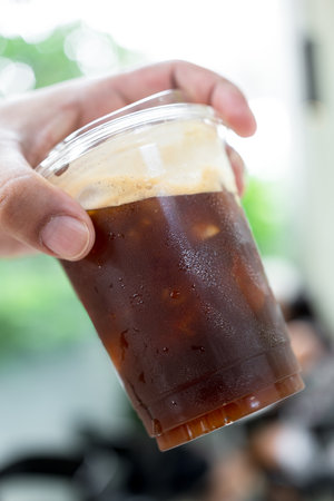 Fresh black coffee with ice in a takeaway plastic glass 16oz. on handの写真素材