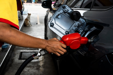 Attendant in uniform at the gas station, filling with petrol a small car, nozzle is in the tank