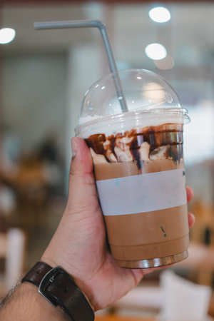Someone hand holding iced mocha coffee in plastic glass with blur coffee shopの写真素材