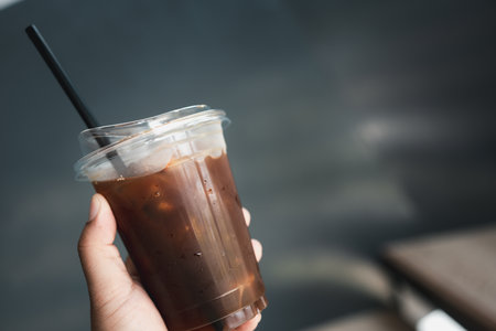 Ice black coffee or Americano in plastic cup with black straw in handの写真素材