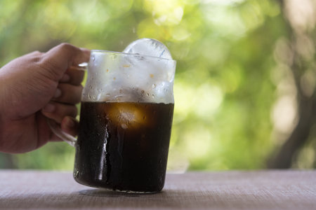 Hand holding black coffee or Americano coffee in a transparent glass mug.