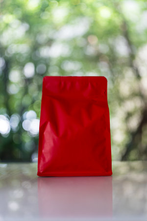 Red pack of coffee against nature background. Mockup coffee bag