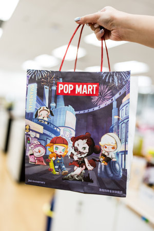 Bangkok, Thailand - September 16, 2024 : Hand holding a white paper shopping bag with red handle from POP MART. POP MART is the largest and fastest growing toy maker in China.のeditorial素材