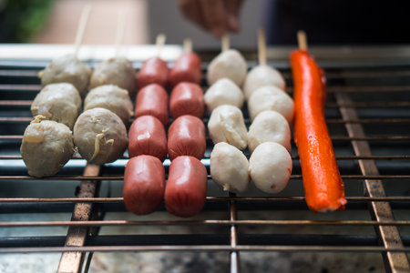 Grilling sausage, and meatballs on a grill on the steel stove on fire at the market. Thai street food.の写真素材