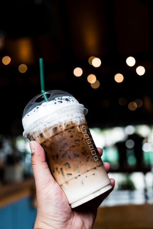 Someone hand holding a plastic cup of iced Mocha coffee and. Ready to go package. Favorite caffeine beverage manuの写真素材