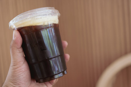 A man hand holding ice black coffee in clear plastic cupの写真素材