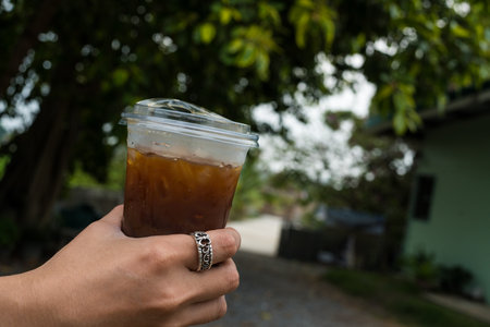 A hand holding a plastic glass of iced black coffee at gardenの写真素材