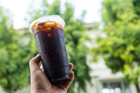 Black Americano coffee cold in to go plastic glass holding in hand on a nature background