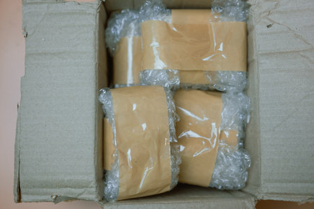 Packing fragile items with plastic air bubble wrapped and adhesive tape and putting in a brown...